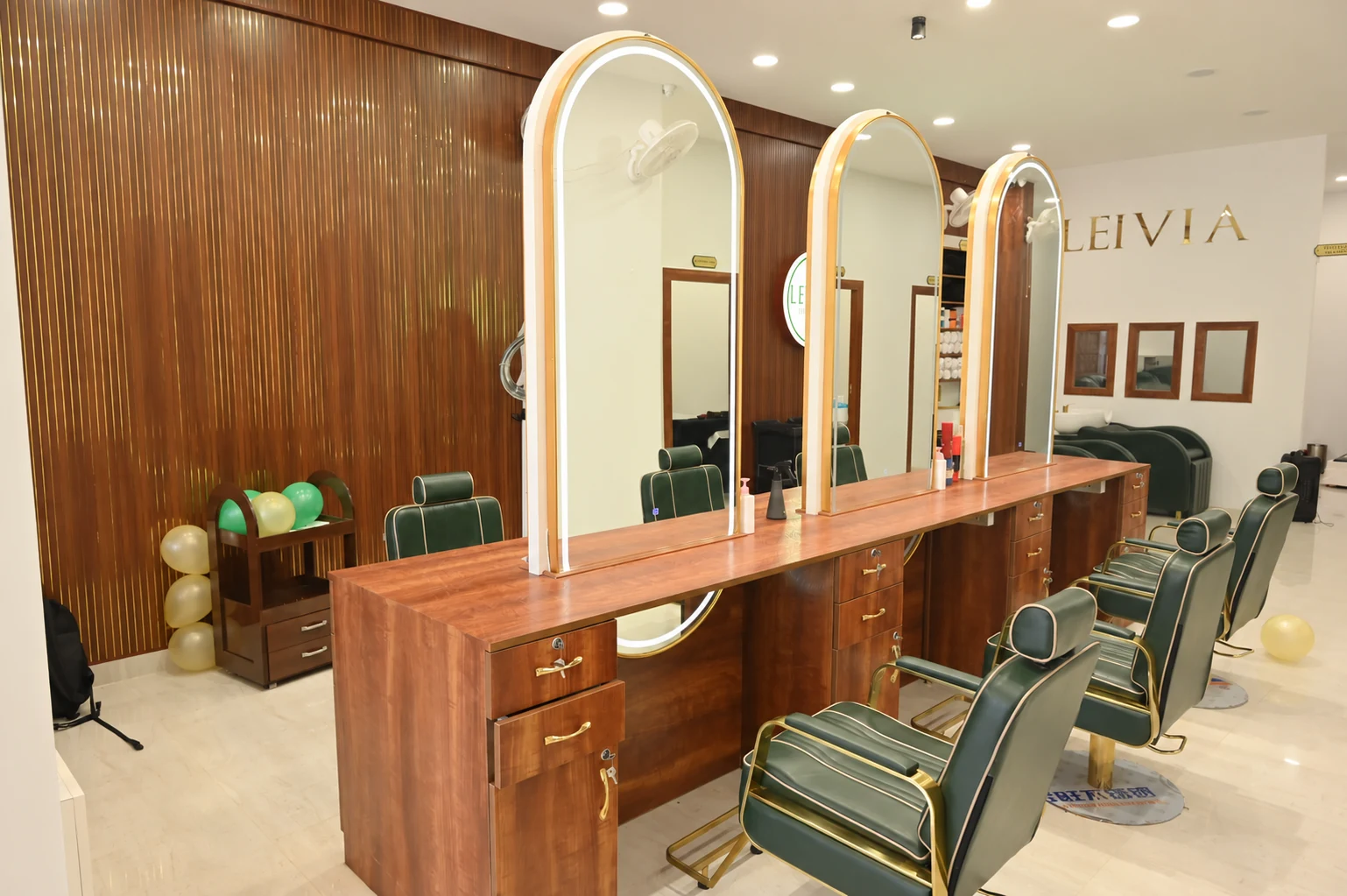 Leivia Salon styling stations with dark green chairs, warm wood and gold details